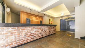 A hotel reception area with a brick wall, a wooden reception desk, and a tiled floor. - H Hotel Ulsan (Ulsan)
