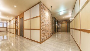 A hotel corridor with a polished tile floor, wooden paneling, and a brick accent wall. - H Hotel Ulsan (Ulsan)