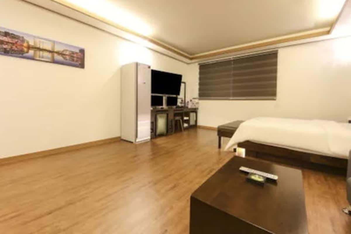 Habitación de hotel con cama, escritorio, silla, televisor y ventana con persianas.