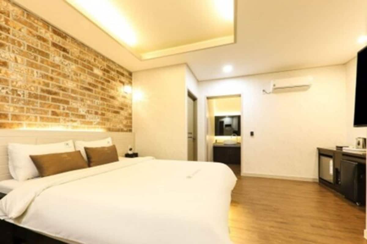 Una habitación de hotel moderna con pared de ladrillo decorativa, una cama grande, un televisor de pantalla plana y una pequeña kitchenette.
