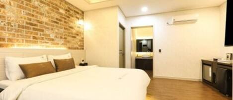 Una habitación de hotel moderna con pared de ladrillo decorativa, una cama grande, un televisor de pantalla plana y una pequeña kitchenette.