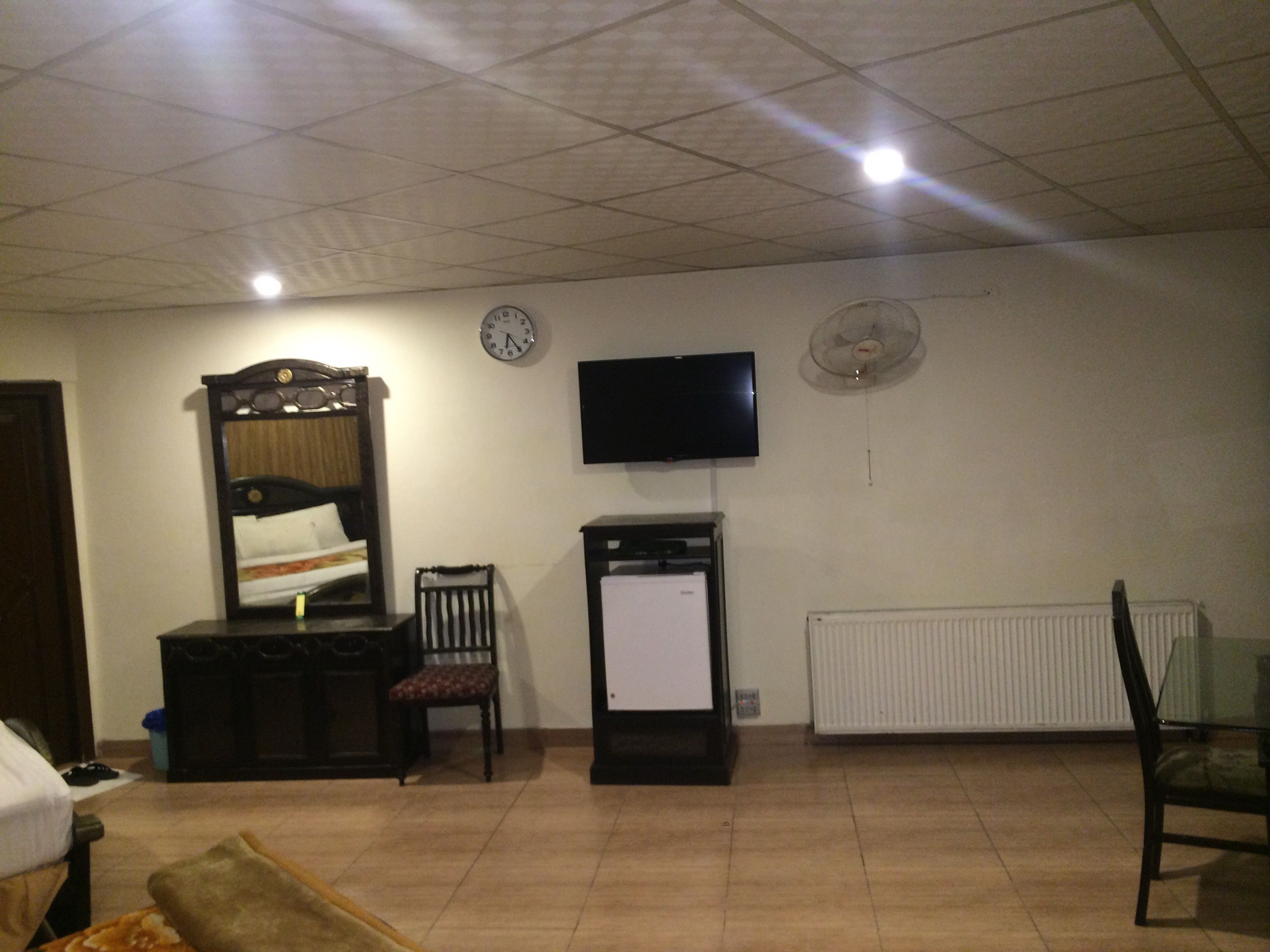 Una camera d'albergo con un letto, una scrivania, una sedia, un televisore, una sveglia e un termosifone.