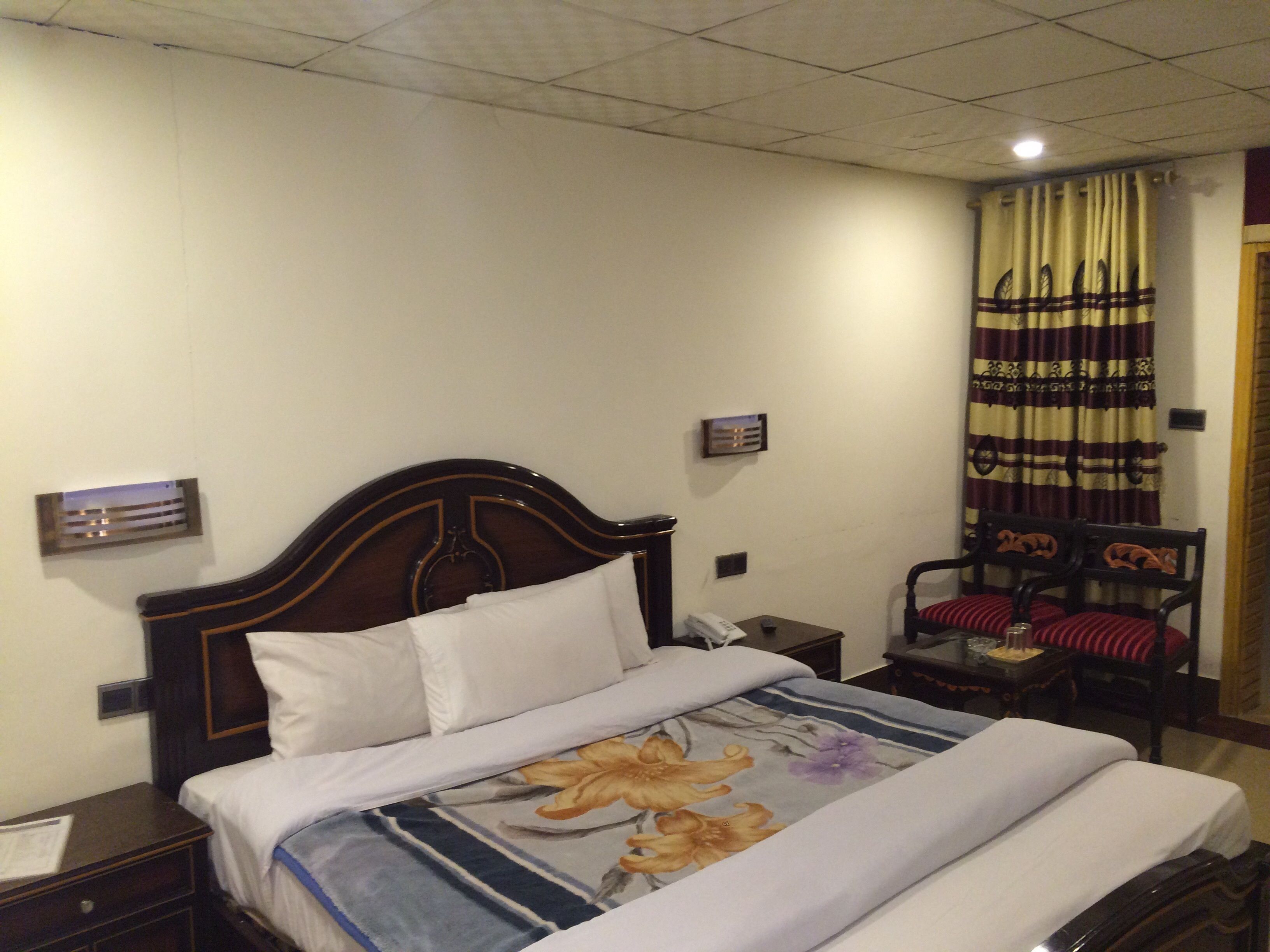 A hotel room with a wooden bed, a nightstand with a telephone, a chair with a red cushion, and a curtain with a striped pattern.