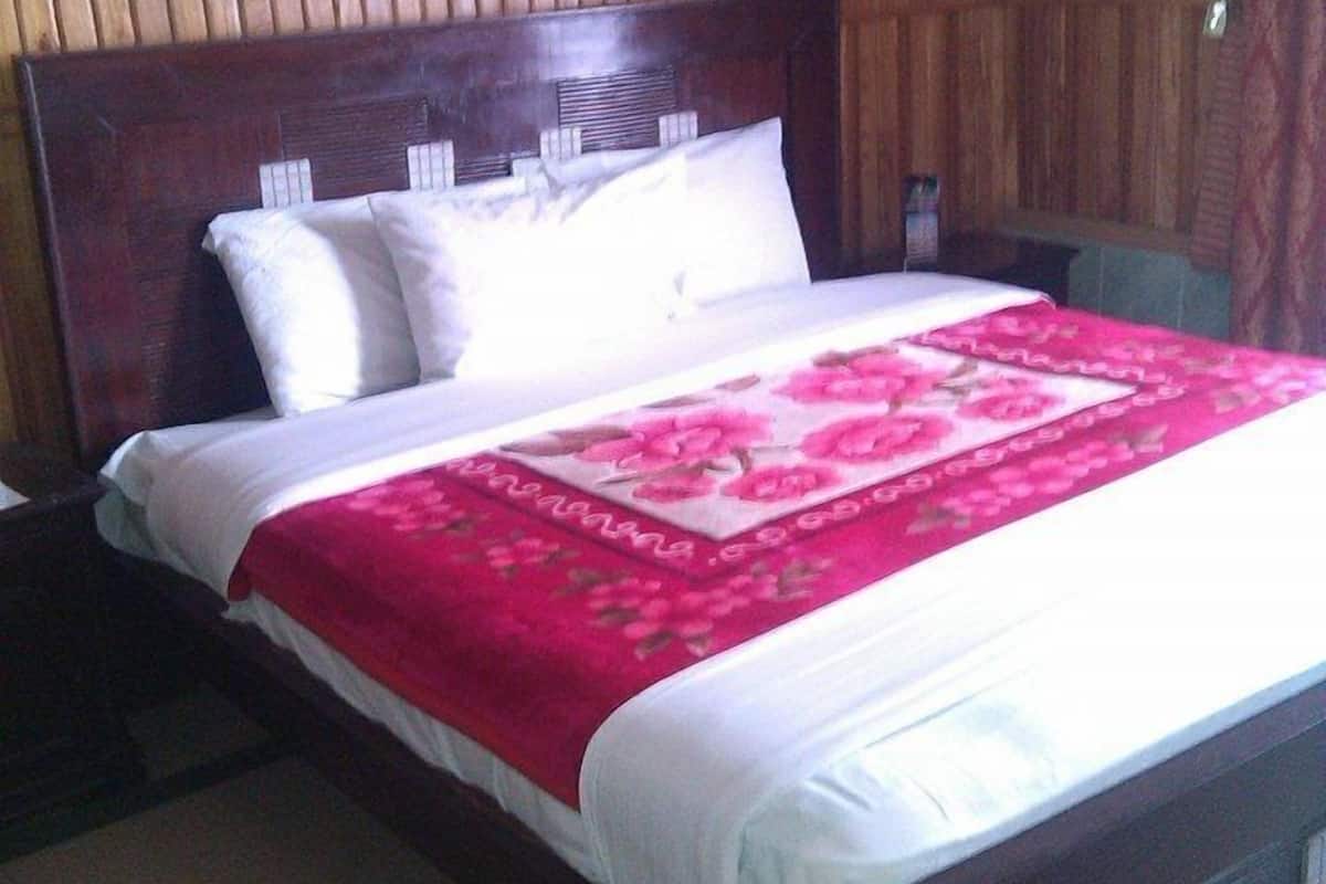 A standard hotel room with a wooden headboard, a large bed with white linens and a red floral bedspread, and a wooden nightstand.