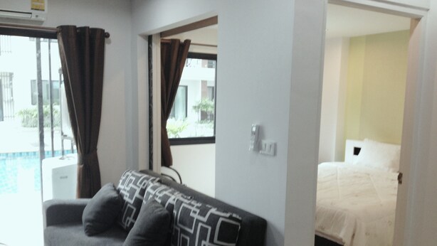 A room with a grey sofa, a bed with white bedding, and a window with curtains. - Ratchaporn Place (Kathu)