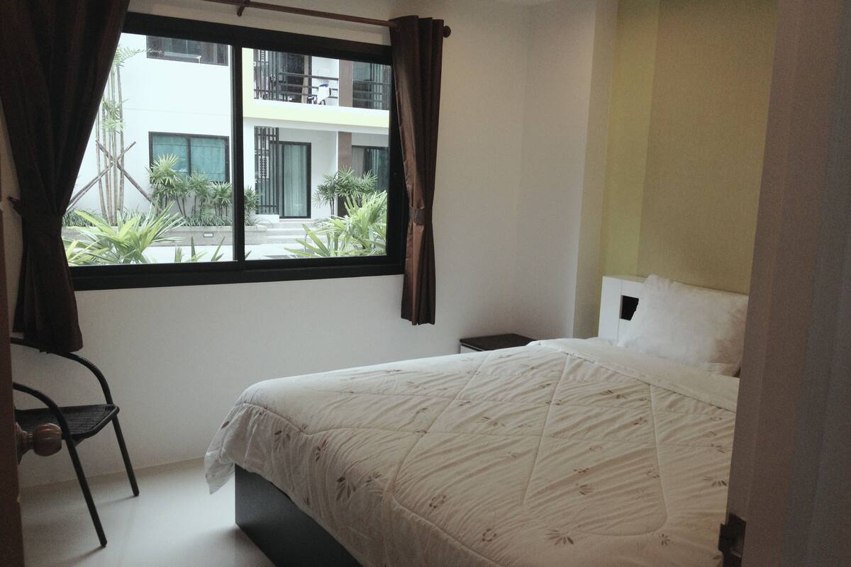 A bedroom with a bed, a chair, a window, and a view of a building outside.