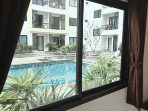 A view of a swimming pool with a tiled floor, surrounded by potted plants and a building with balconies in the background. - Ratchaporn Place (Kathu)