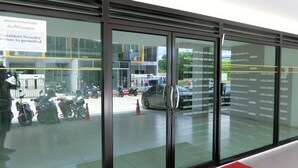 A modern building entrance with glass doors, a sign prohibiting outsiders from entry, and a parking area with motorcycles and cars. - Ratchaporn Place (Kathu)