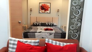 A hotel room with a bed, a red and white checkered pillow, a red pillow, a wall with a red flower painting, and a grey wall with circular patterns. - Ratchaporn Place (Kathu)