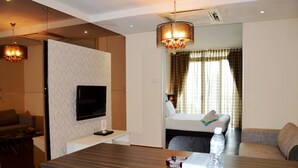 Habitación de hotel con televisor de pantalla plana en la pared, escritorio de madera con una botella de agua, sofá y cama con una manta blanca.
