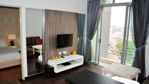 Habitación de hotel con cama, sofá, televisión, una mesita y balcón con cortinas.