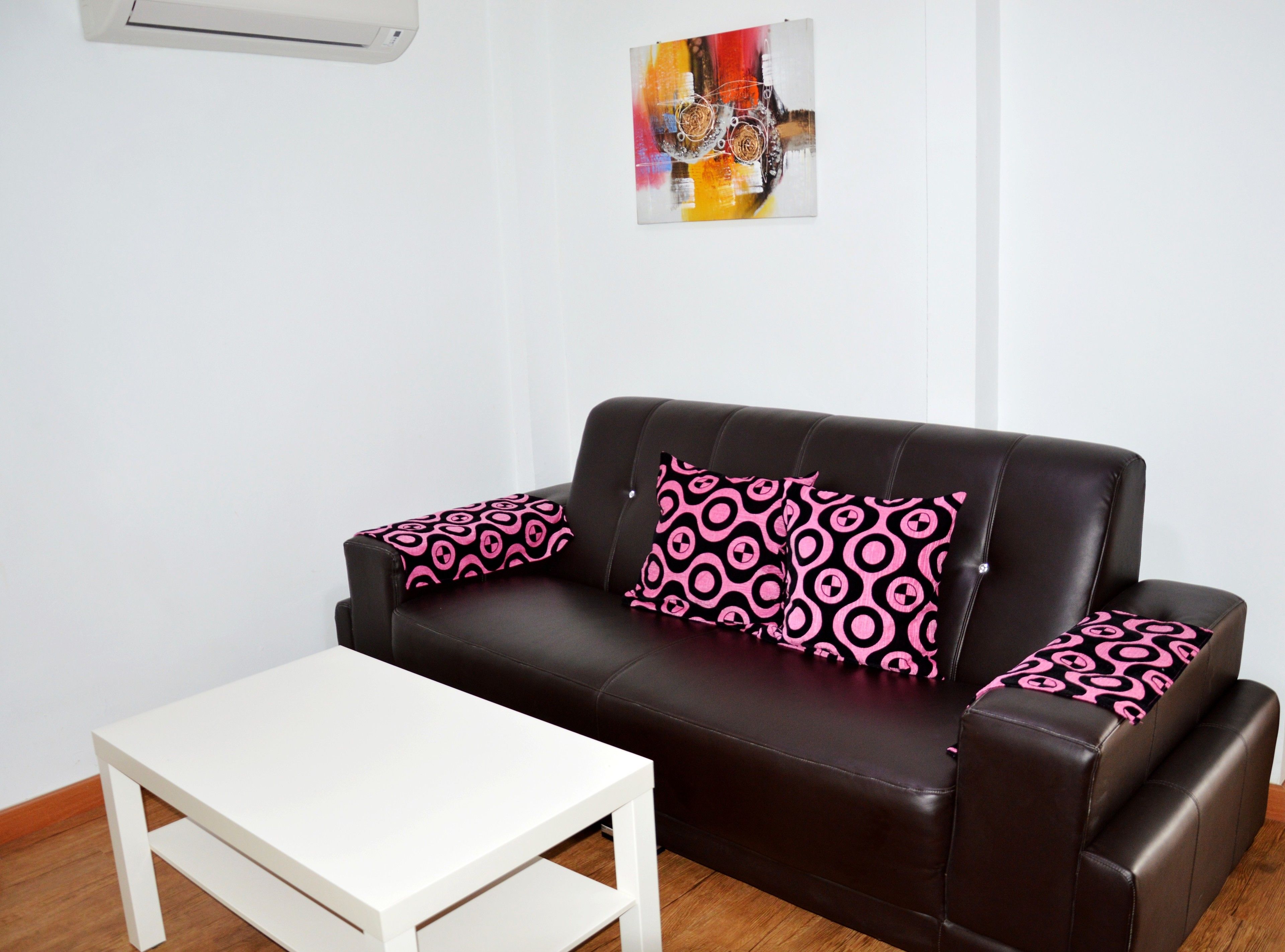 Una sala de estar con un sofá de cuero marrón, dos almohadones rosados estampados a juego y una mesa de centro blanca.
