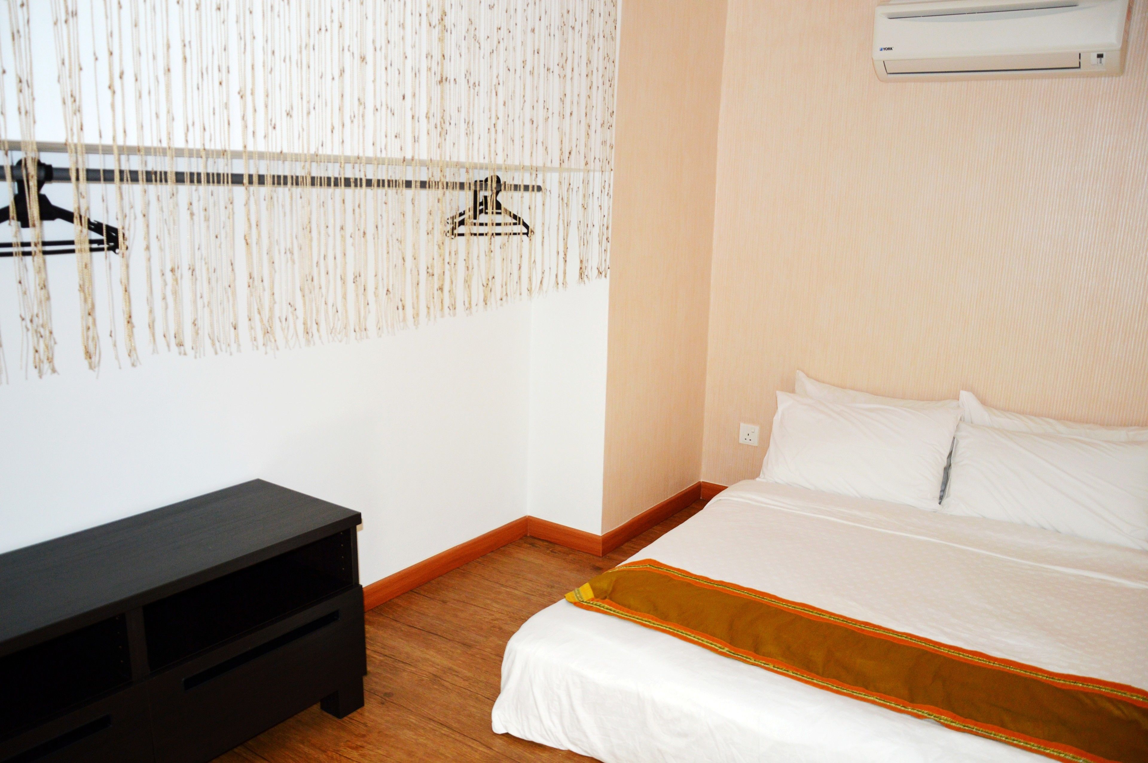 A hotel room with a bed, a black nightstand, a wall-mounted air conditioner, and a wooden floor.