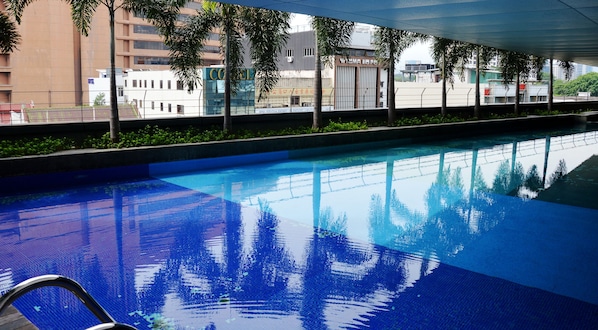 Una piscina con agua azul cristalina, rodeada de vegetación y edificios modernos.