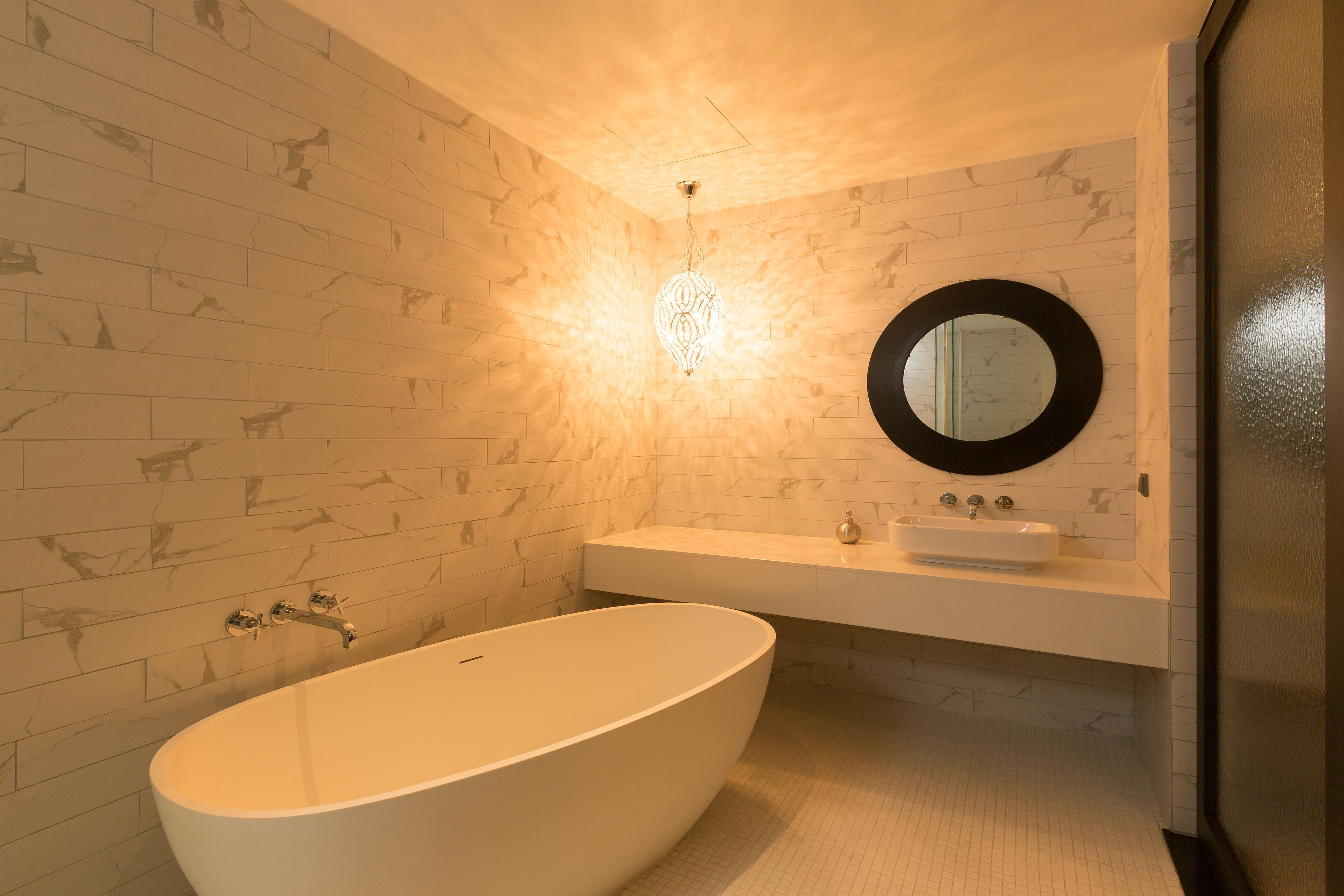 Een moderne badkamer met een vrijstaand bad, een ronde spiegel en een lamp boven de wastafel.