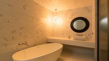 Een moderne badkamer met een vrijstaand bad, een ronde spiegel en een lamp boven de wastafel.