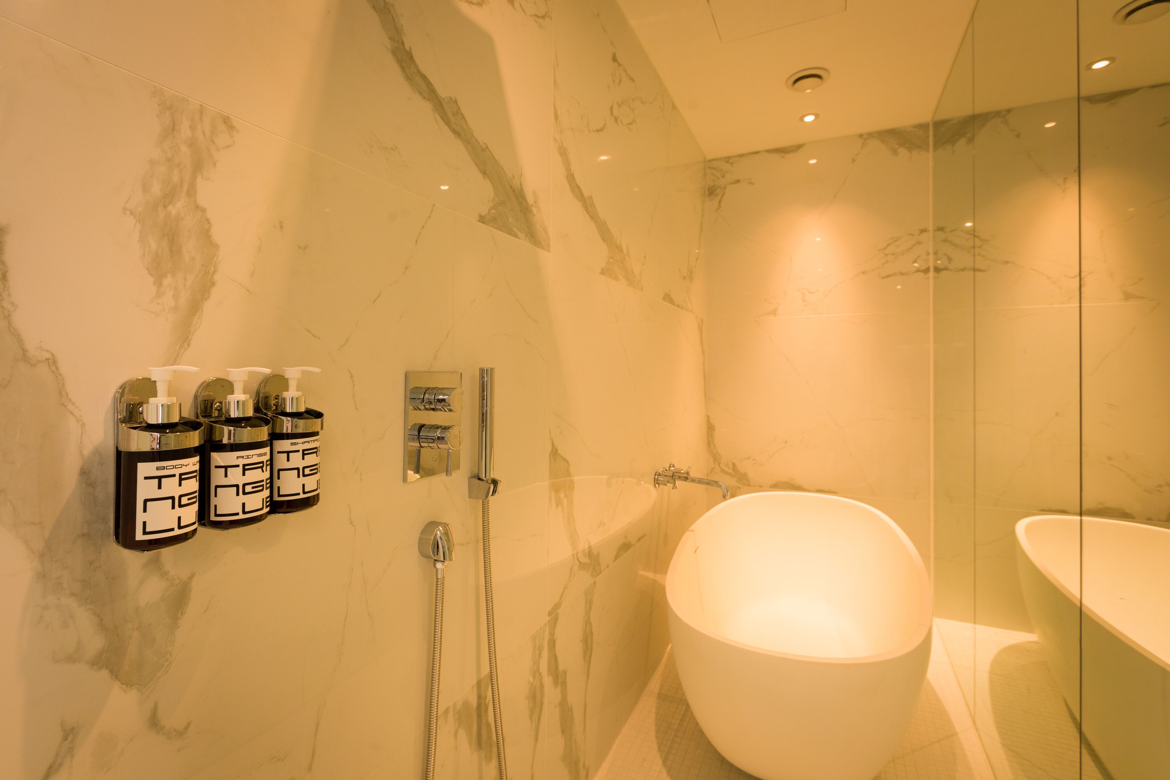Un baño moderno con una bañera grande, un box de ducha de vidrio y tres botellas de jabón de manos en la pared.
