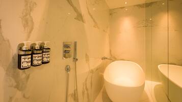 Un baño moderno con una bañera grande, un box de ducha de vidrio y tres botellas de jabón de manos en la pared.