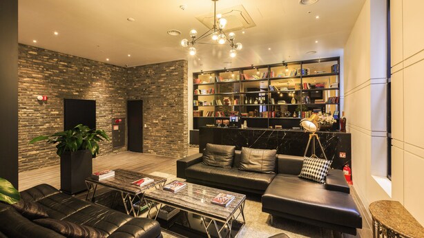 A modern lounge area with leather sofas, a coffee table, a bookshelf, and a potted plant. - Trang BLUE (Seoul)