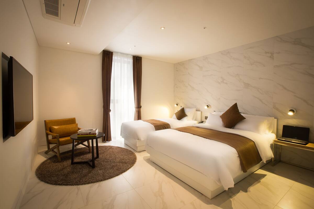 A hotel room with two beds, a desk, a chair, and a TV.
