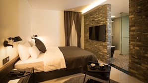A modern hotel room with a large bed, a flat-screen TV mounted on a brick wall, a bedside telephone, and a small table with a cup and saucer. - Trang BLUE (Seoul)