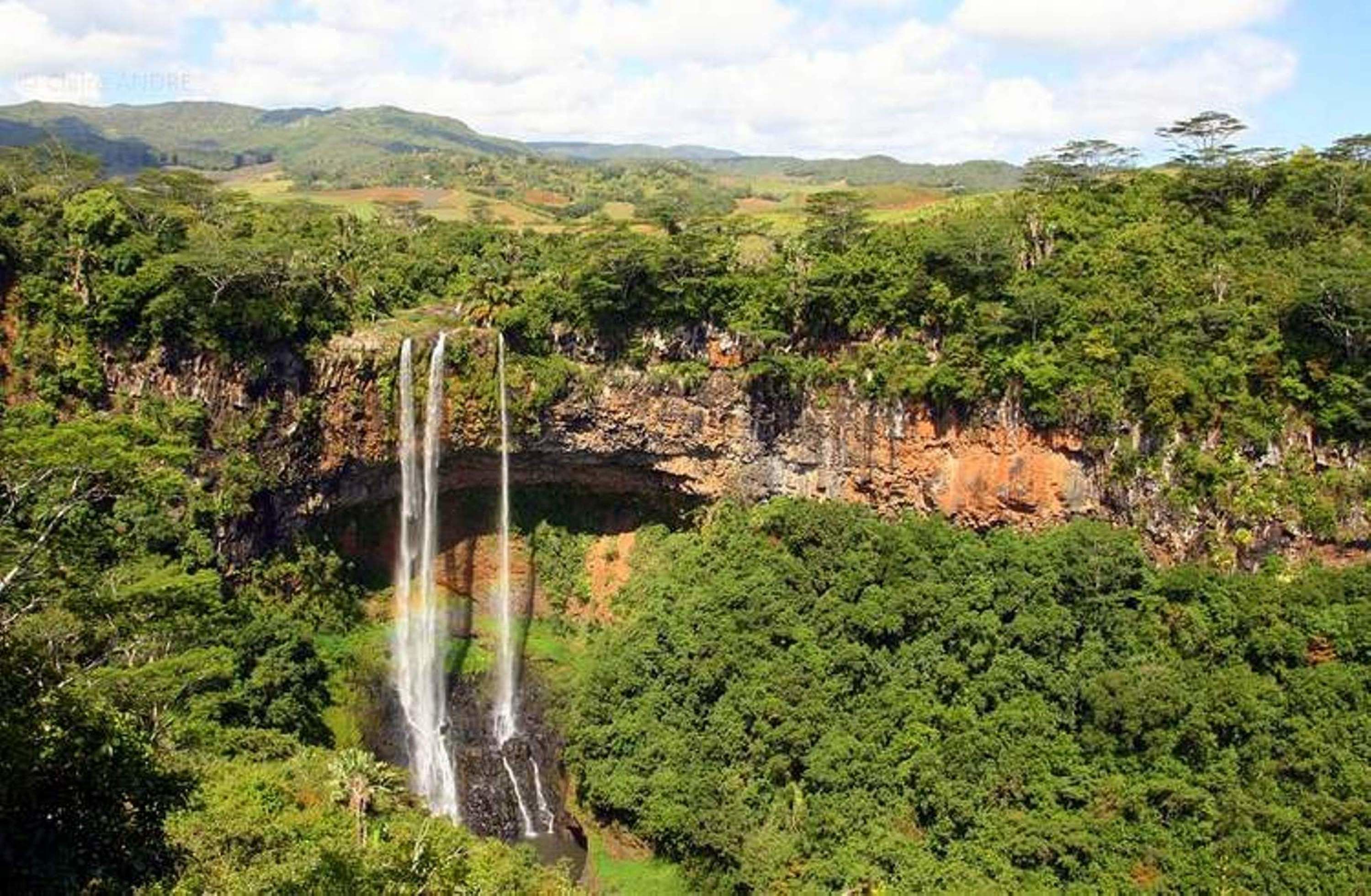 A waterfall surrounded by lush greenery and hills in the background.