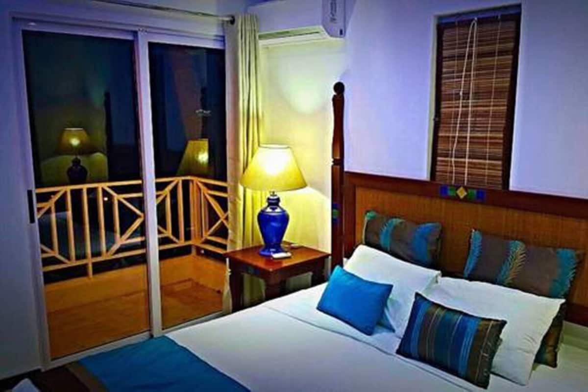 Hotelkamer met een bed, nachtkastje met lamp, balkon met hekwerk en raam met jaloezieën.