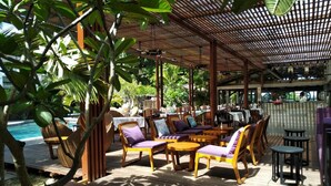 An outdoor seating area with wooden furniture and a pool in the background. - Ocean Villas Apart Hotel (Grand-Baie)