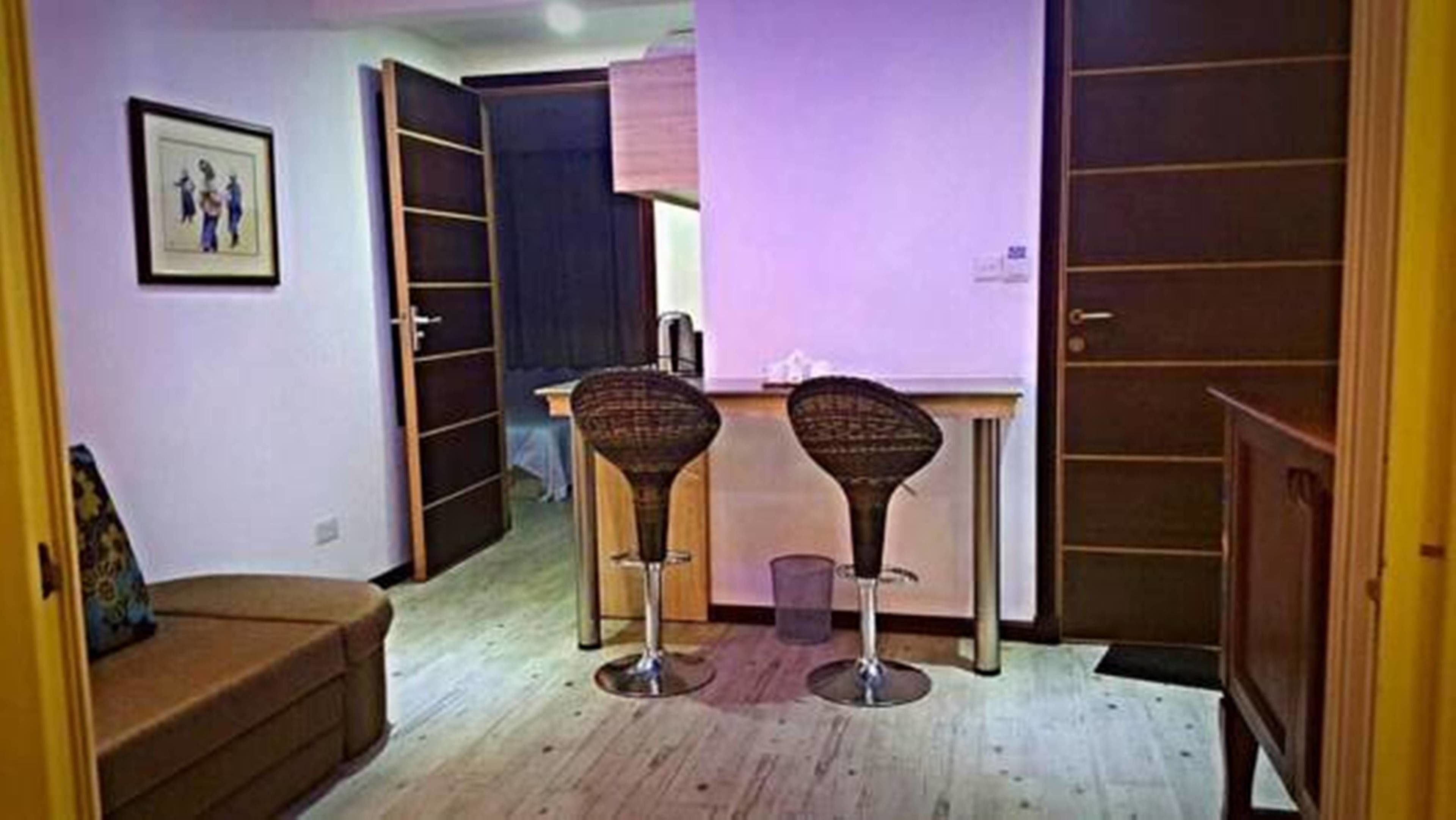 A compact living space with a kitchenette, two bar stools, a sofa, and a wardrobe.