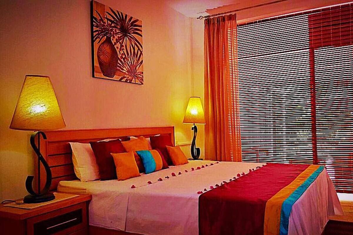 Een hotelkamer met een bed, twee bedlampjes, een raam met luxaflex en een schilderij aan de muur.