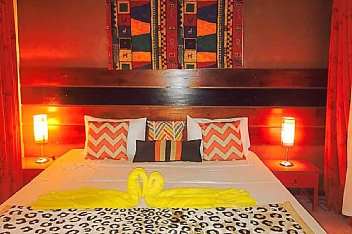 Een hotelkamer met een bed, twee bedlampen, een decoratieve wandhanger en een bedsprei met luipaardprint.