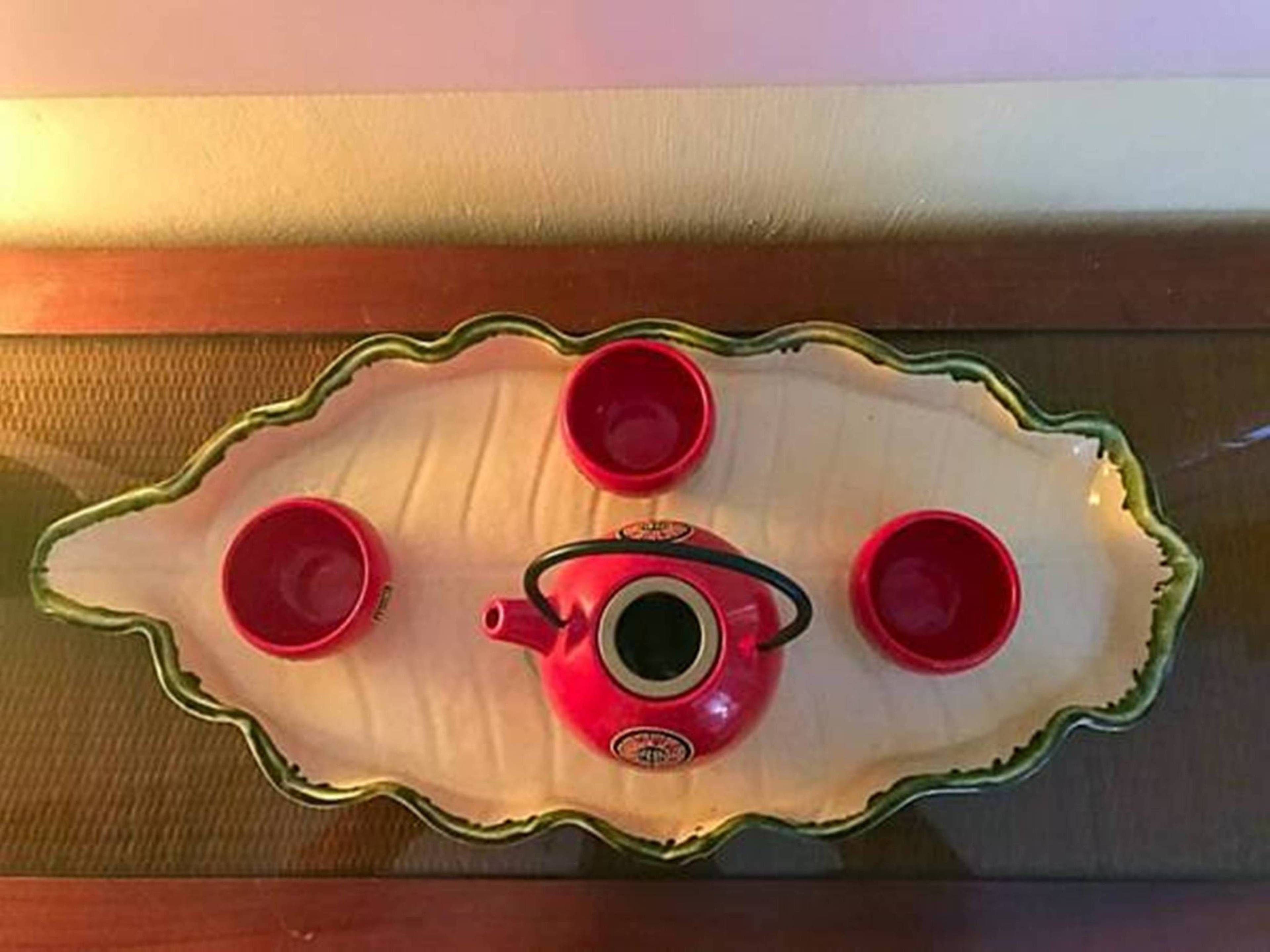 A table with a decorative plate holding four red cups and a teapot.
