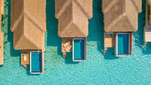 Vue aérienne de bungalows sur pilotis dotés de piscines privées et de chaises longues en bois.