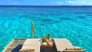 Une terrasse en bois avec deux chaises longues et une table sur laquelle se trouve un saladier rempli de fruits.