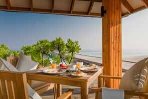 Mesa de madeira posta para o café da manhã, com vista para a praia e o oceano.