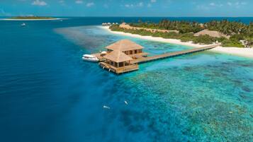 An overwater bungalow with a thatched roof, connected to the beach by a wooden walkway.