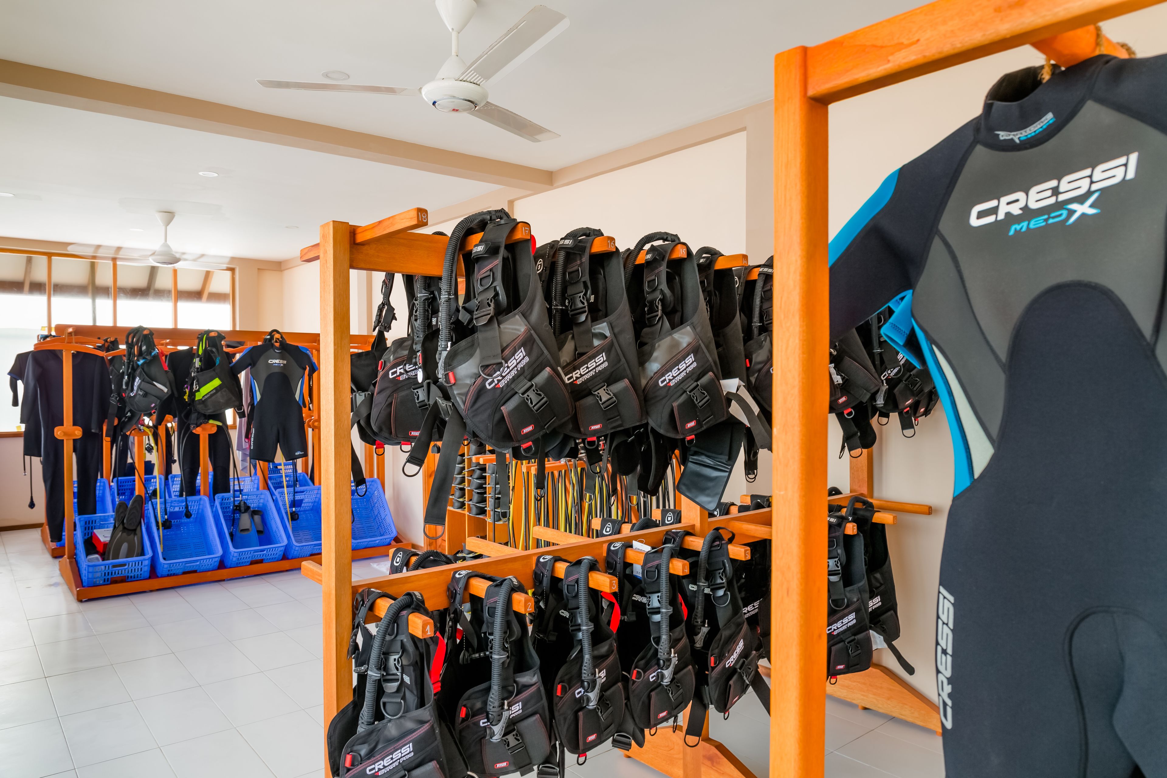 A store with rows of black and orange diving gear, including wetsuits and bags, on wooden racks.