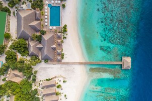 An aerial view of a resort with a swimming pool, beach, and a long pier extending into the ocean.