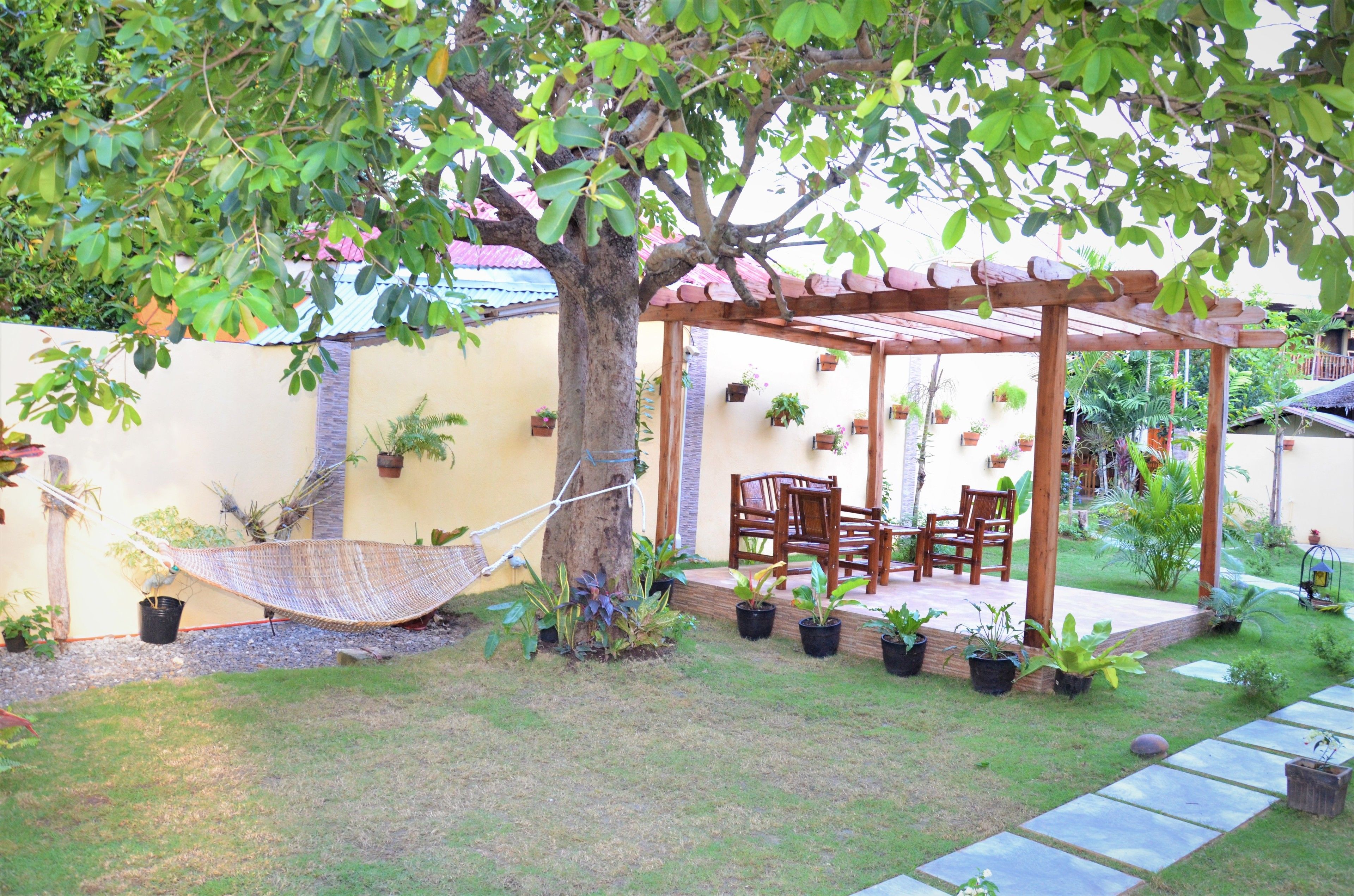 A covered patio area with a hammock, wooden chairs, and potted plants.