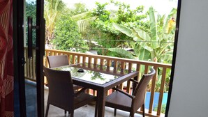 An outdoor balcony with a glass-top table and wicker chairs, surrounded by lush greenery and a wooden railing. - Captain's Lodge and Bar (Panglao)