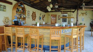 A bar area with wooden chairs, a bar counter, and a shelf with bottles. - Captain's Lodge and Bar (Panglao)