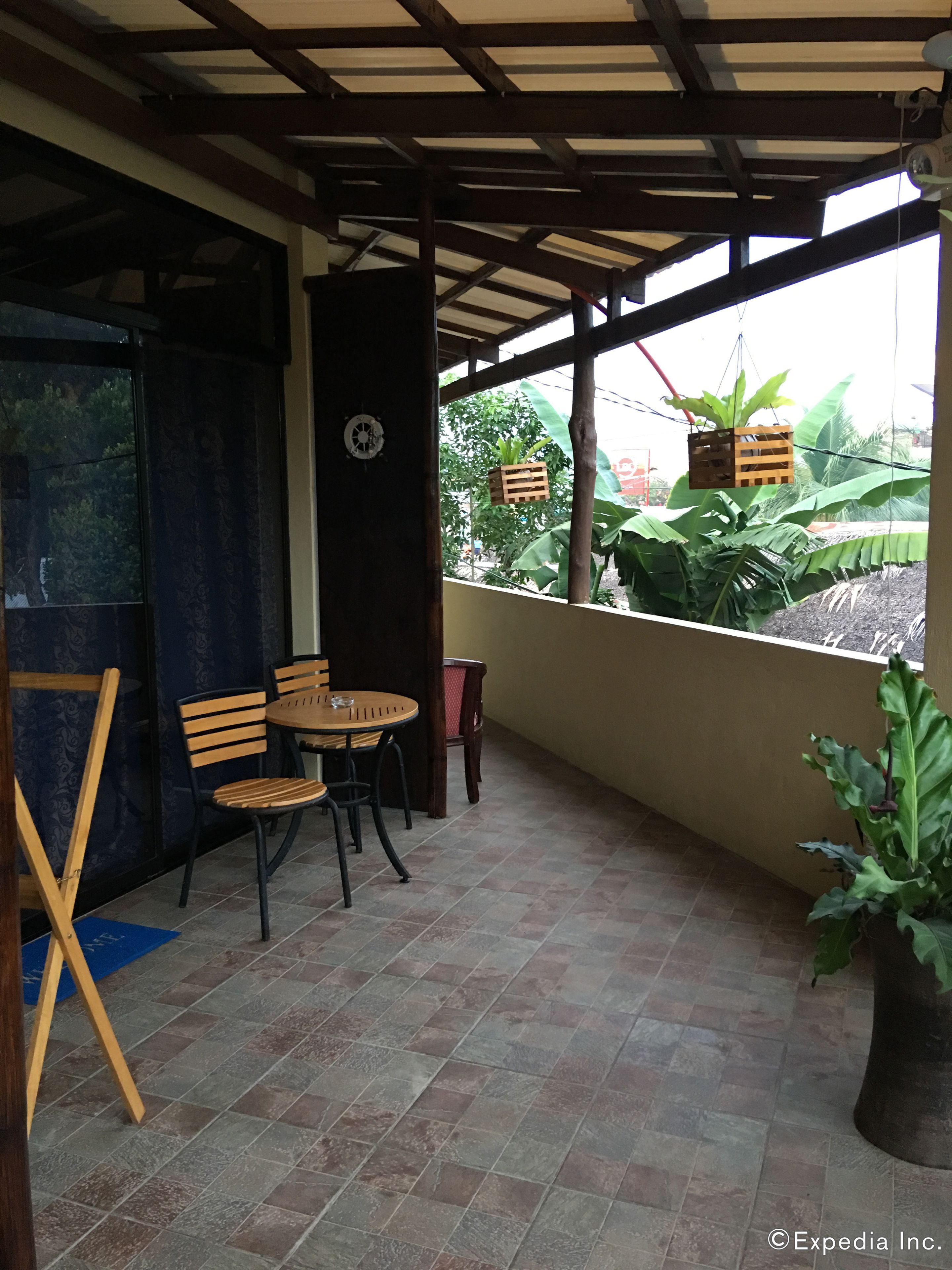 A covered patio area with a table and chairs, a potted plant, and a view of greenery outside.