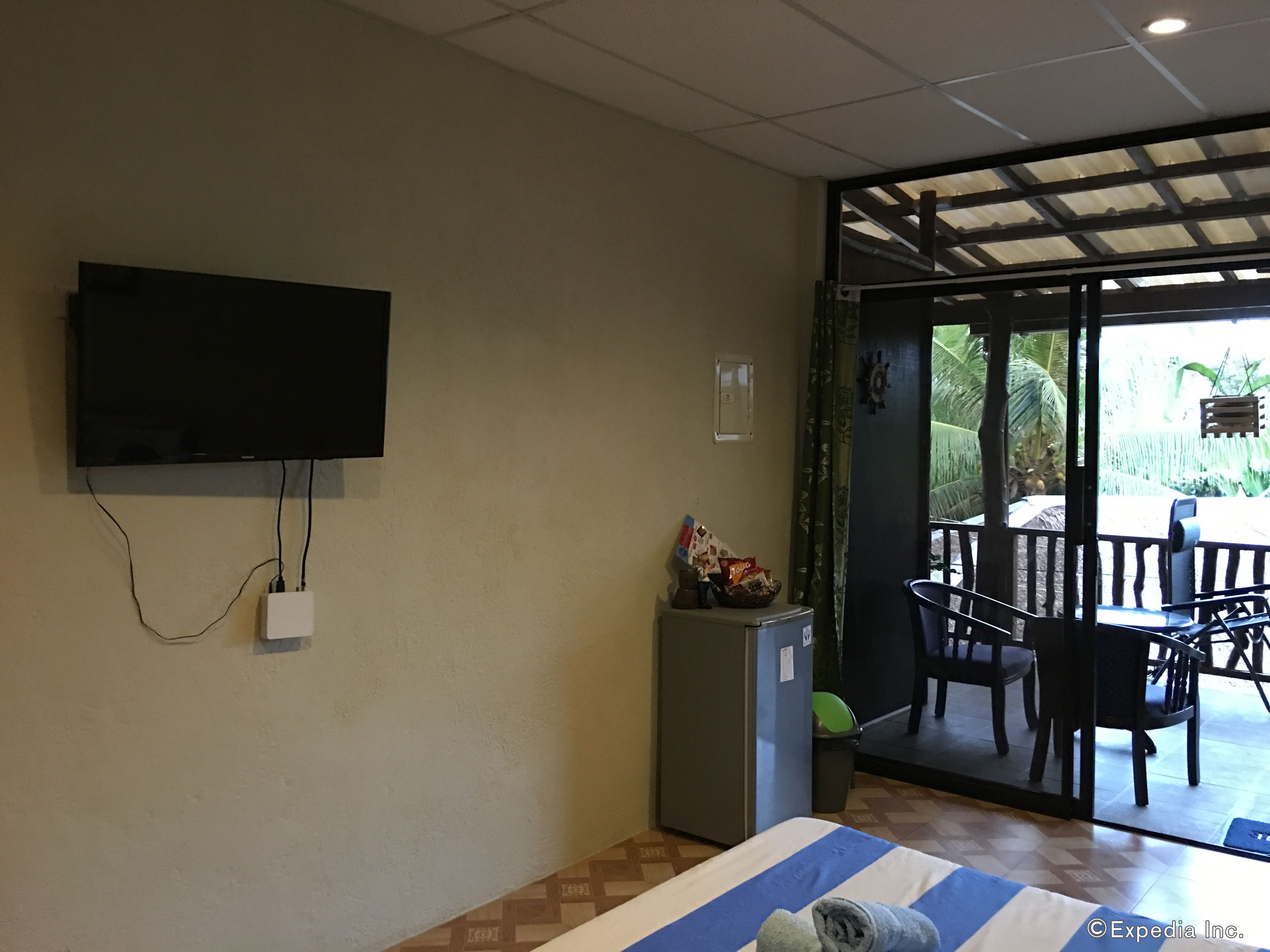 Een hotelkamer met een bed, een televisie aan de muur, een kleine koelkast en uitzicht op een terras met stoelen en een tafel.