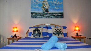 A hotel room with a bed featuring blue and white striped bedding, two nightstands with lamps, and a painting of a sailing ship on the wall. - Captain's Lodge and Bar (Panglao)
