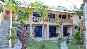 A two-story building with a balcony, a stone staircase, and a well-maintained garden with various plants. - Captain's Lodge and Bar (Panglao)