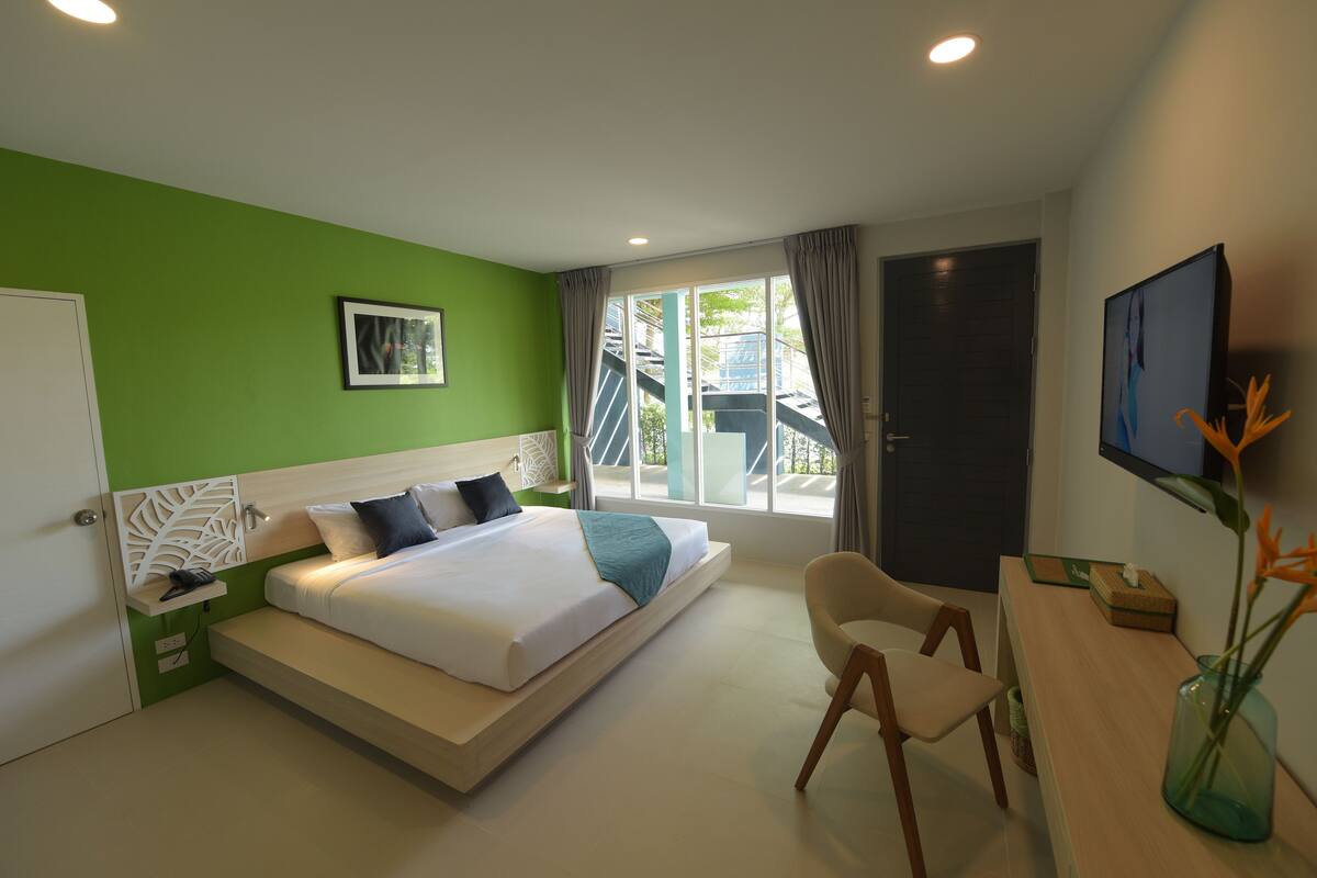A modern hotel room with a large bed, a desk, a chair, and a view of the outside.