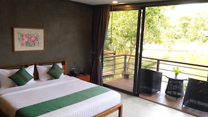 A hotel room with a large bed, a small table, a chair, and a balcony with a view of greenery and a body of water. - The Touch Green Naiyang Hotel & Fitness (Sa Khu)