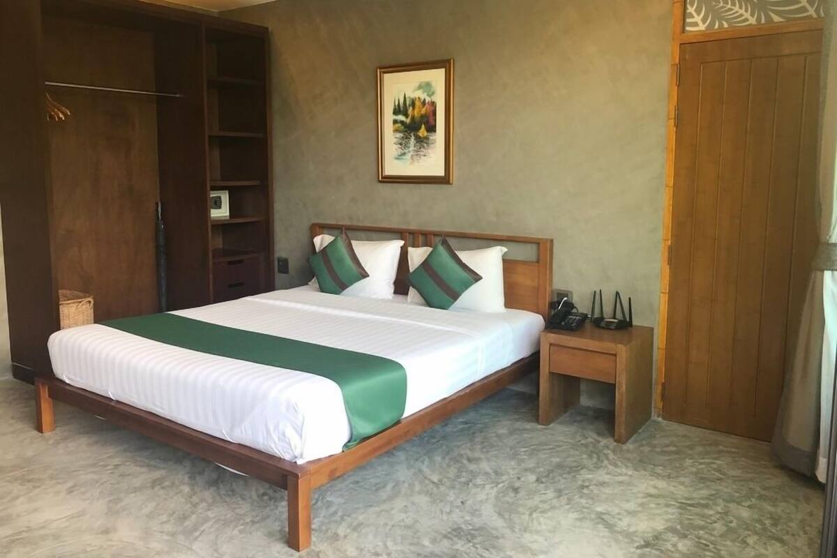 A bedroom with a large bed, a wooden wardrobe, a small bedside table, and a wall-mounted shelf.