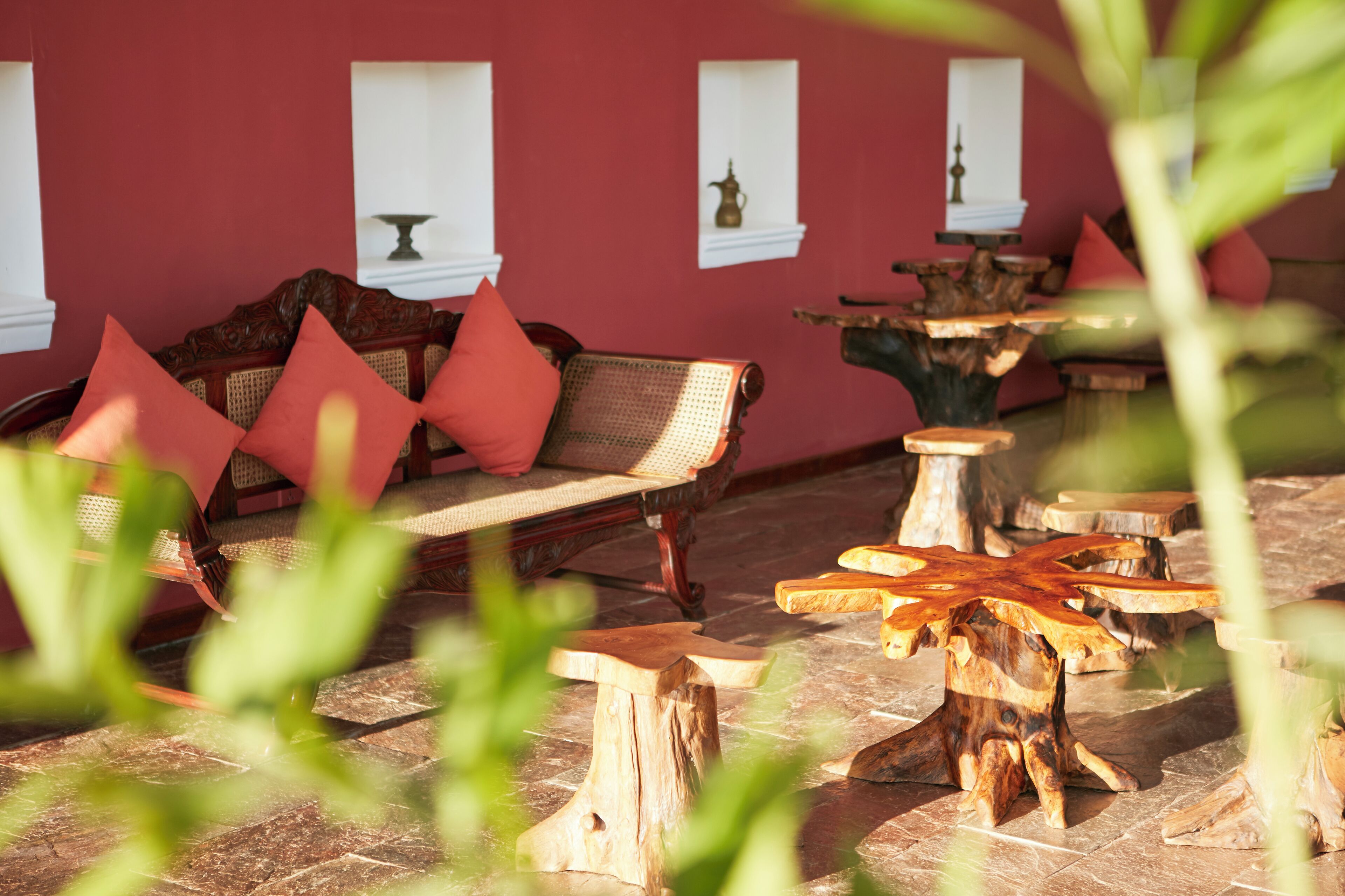 A red-walled room with a wooden bench and a table, surrounded by wooden stools.