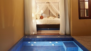 A bedroom with a bed under a canopy, a blue-tiled bathtub, and a wooden floor. - Seerock The King's Domain (Avudangawa)